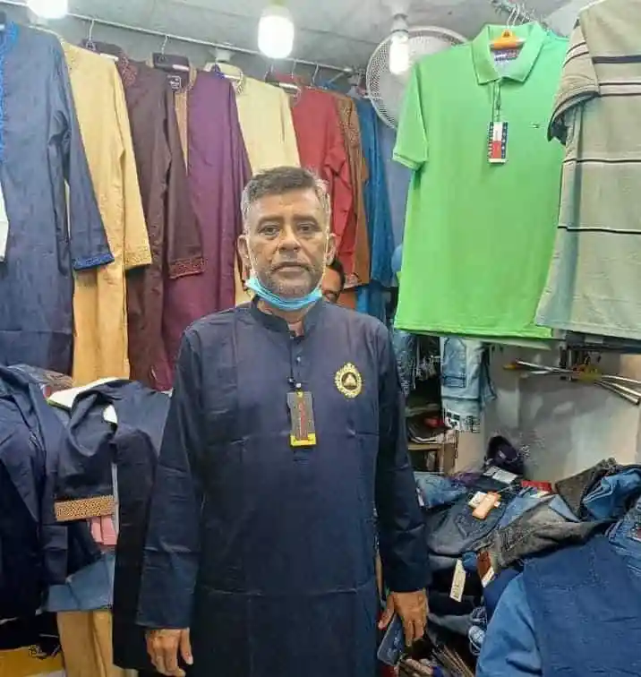 বাজারে পোশাক বিক্রেতা, বিভিন্ন রঙের শার্ট ও প্যান্টের পেছনে. Channel i News - চ্যানেল আই নিউজ