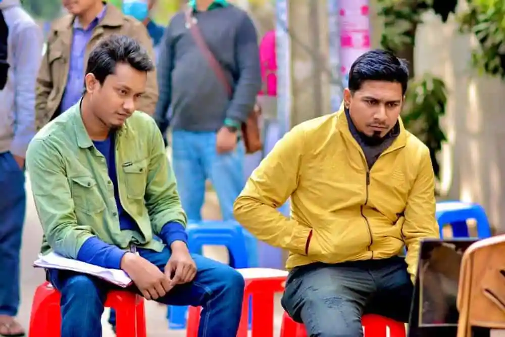 দুটি যুবক বসে আছেন, একজন বই পড়ছেন, অন্যজন ভাবছেন. Channel i News - চ্যানেল আই নিউজ