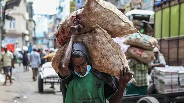 ব্যস্ত শহরে একজন ব্যক্তি ভারী বস্তা বহন করছেন. Channel i News - চ্যানেল আই নিউজ