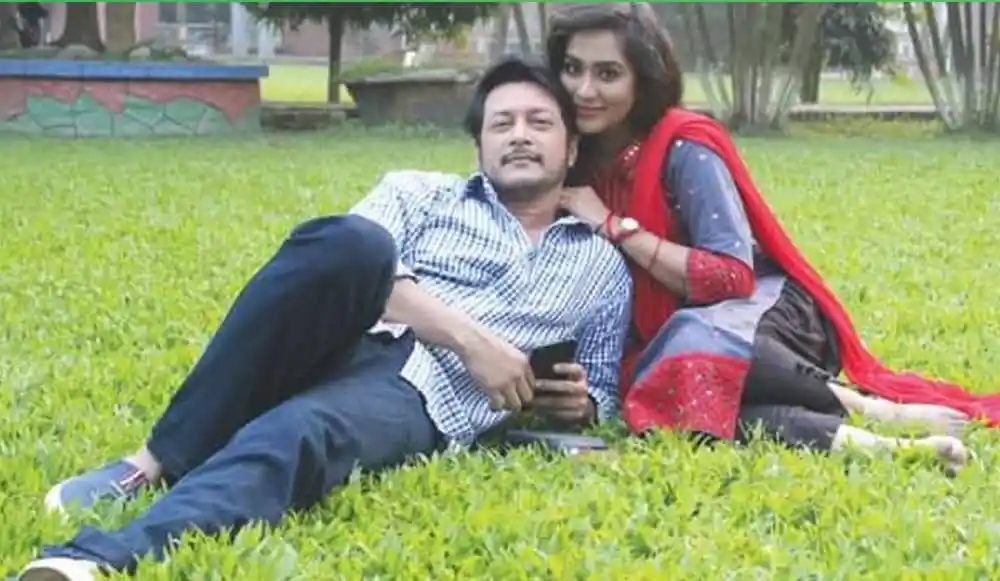 একজন পুরুষ ও একজন নারী বসে আছেন ঘাসের উপর, হাসি মুখে. Channel i News - চ্যানেল আই নিউজ