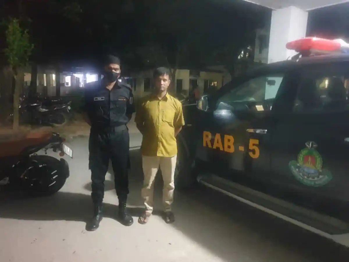 অভিযুক্ত ব্যক্তি ও পুলিশ সদস্যের ছবি, র্যাবের গাড়ি পাশে দাঁড়িয়ে. Channel i News - চ্যানেল আই নিউজ