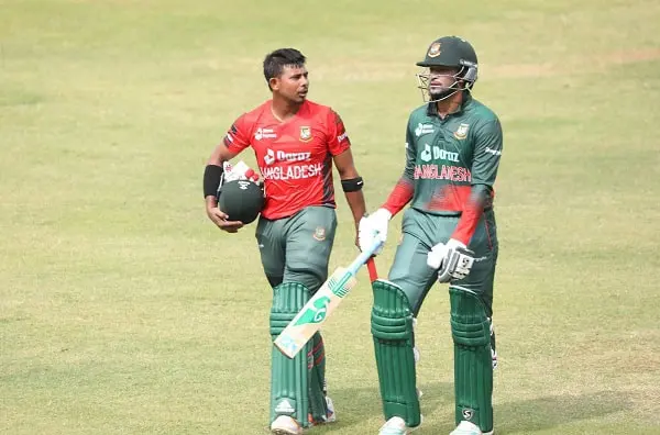 বাংলাদেশ ক্রিকেটাররা মাঠে প্রস্তুত, একজন হাতে ব্যাট ও অন্যজন হেলমেট ধারণ করছেন।. Channel i News - চ্যানেল আই নিউজ