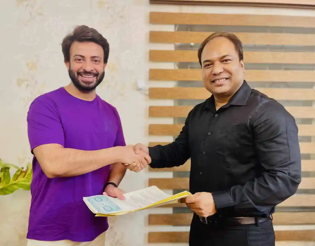 দুই ব্যক্তি হাত মেলাচ্ছেন, একজনের হাতে কাগজ রয়েছে. Channel i News - চ্যানেল আই নিউজ