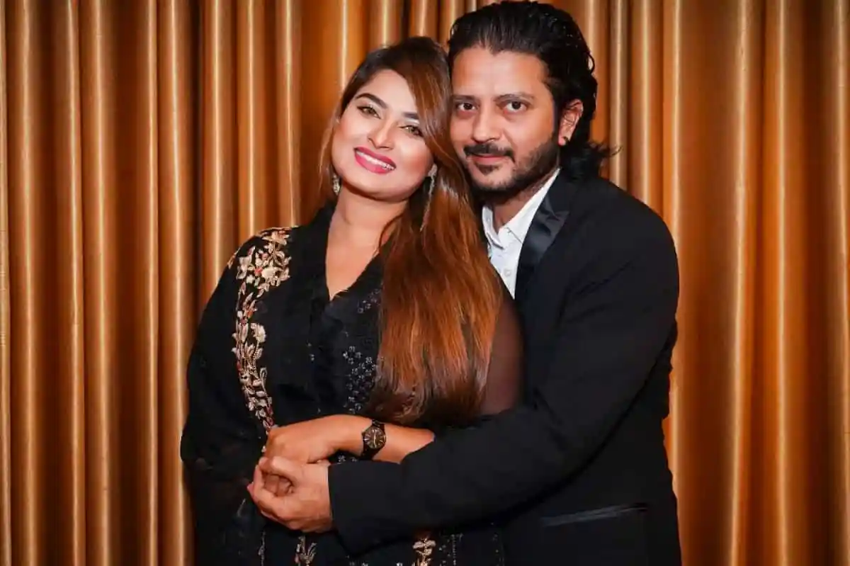 দুটি মানুষ হাসিমুখে একসঙ্গে ছবি তুলছেন, পটভূমিতে বাদামী পর্দা।. Channel i News - চ্যানেল আই নিউজ