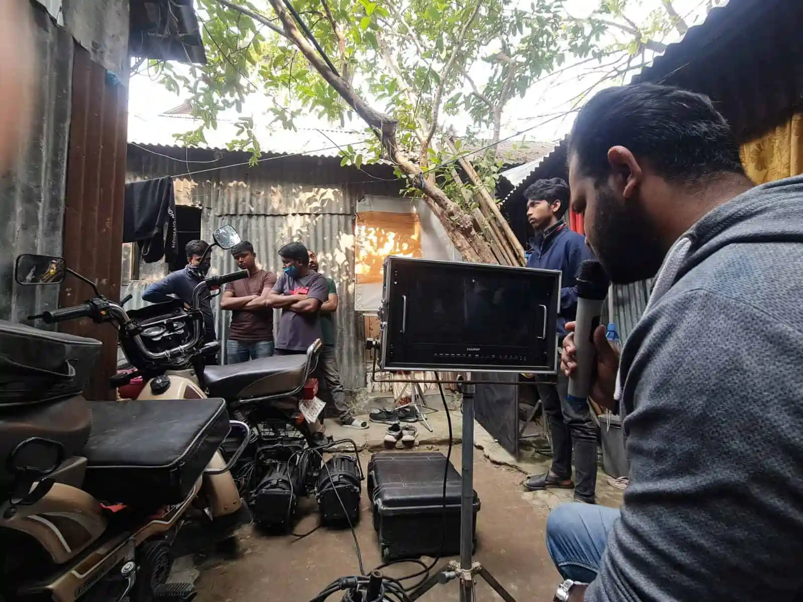 Filming crew capturing scene outdoors with motorcycle and crew members. Channel i News - চ্যানেল আই নিউজ