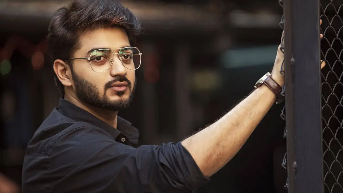 আত্মবিশ্বাসী যুবক কালো পোশাক ও চশমা পরা, শহরের পেছনে দাঁড়িয়ে. Channel i News - চ্যানেল আই নিউজ