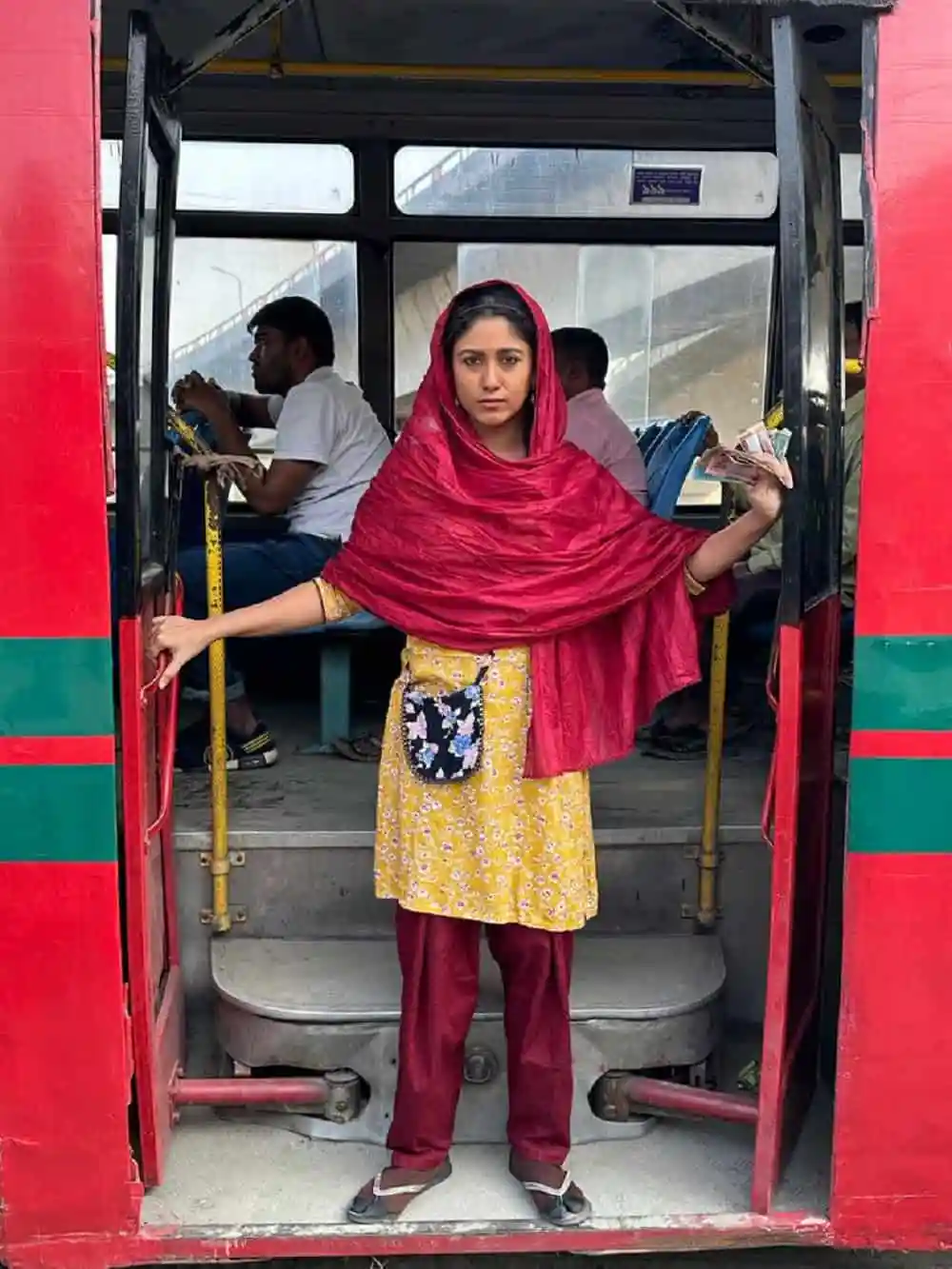 একজন তরুণী বাসের দরজায় দাঁড়িয়ে আছেন, পেছনে অন্য যাত্রীরা বসে আছেন।. Channel i News - চ্যানেল আই নিউজ