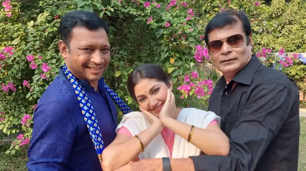 তিনজন মানুষ হাসিমুখে ফুলের বাগানে ছবি তুলছেন. Channel i News - চ্যানেল আই নিউজ