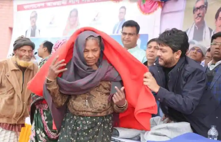 শীতবস্ত্র বিতরণ অনুষ্ঠানে একজন নারী শীতের পোশাক পরছেন. Channel i News - চ্যানেল আই নিউজ