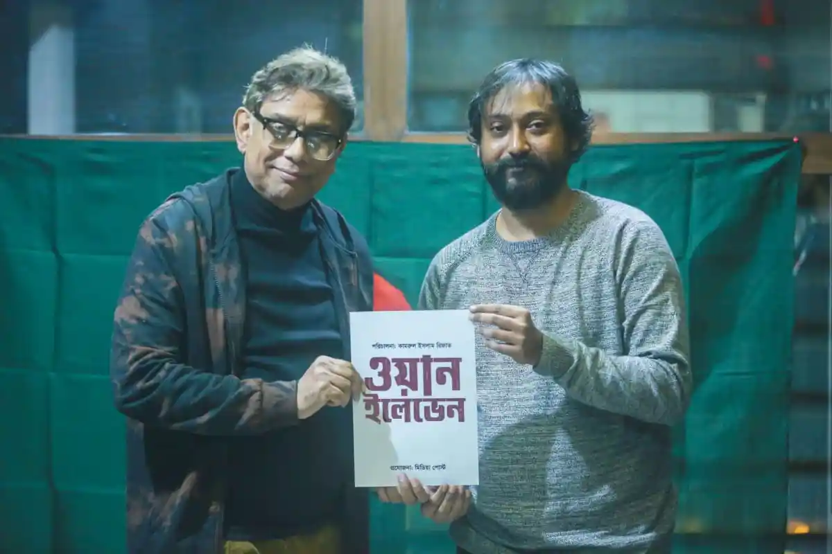 দুই ব্যক্তি বই হাতে নিয়ে ছবি তুলছেন, পেছনে সবুজ পর্দা।. Channel i News - চ্যানেল আই নিউজ