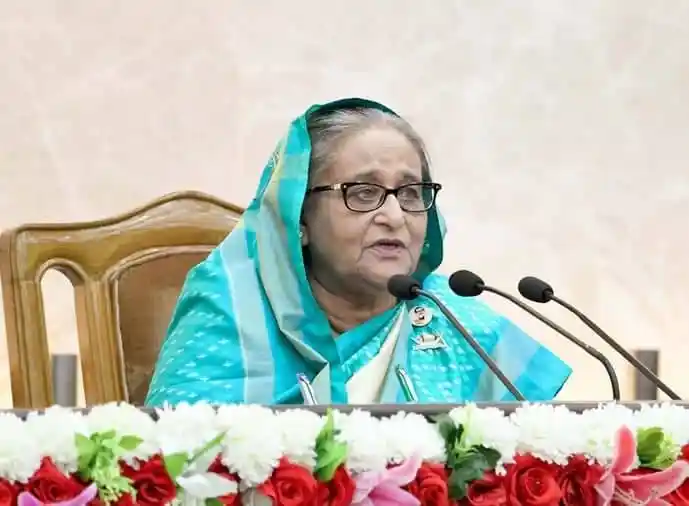 প্রধানমন্ত্রী speaking at a press conference with microphones in front. Channel i News - চ্যানেল আই নিউজ
