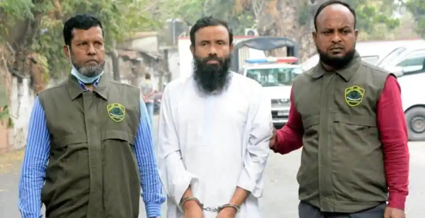 Three men standing outdoors, two wearing green vests with badges, one in white. Channel i News - চ্যানেল আই নিউজ
