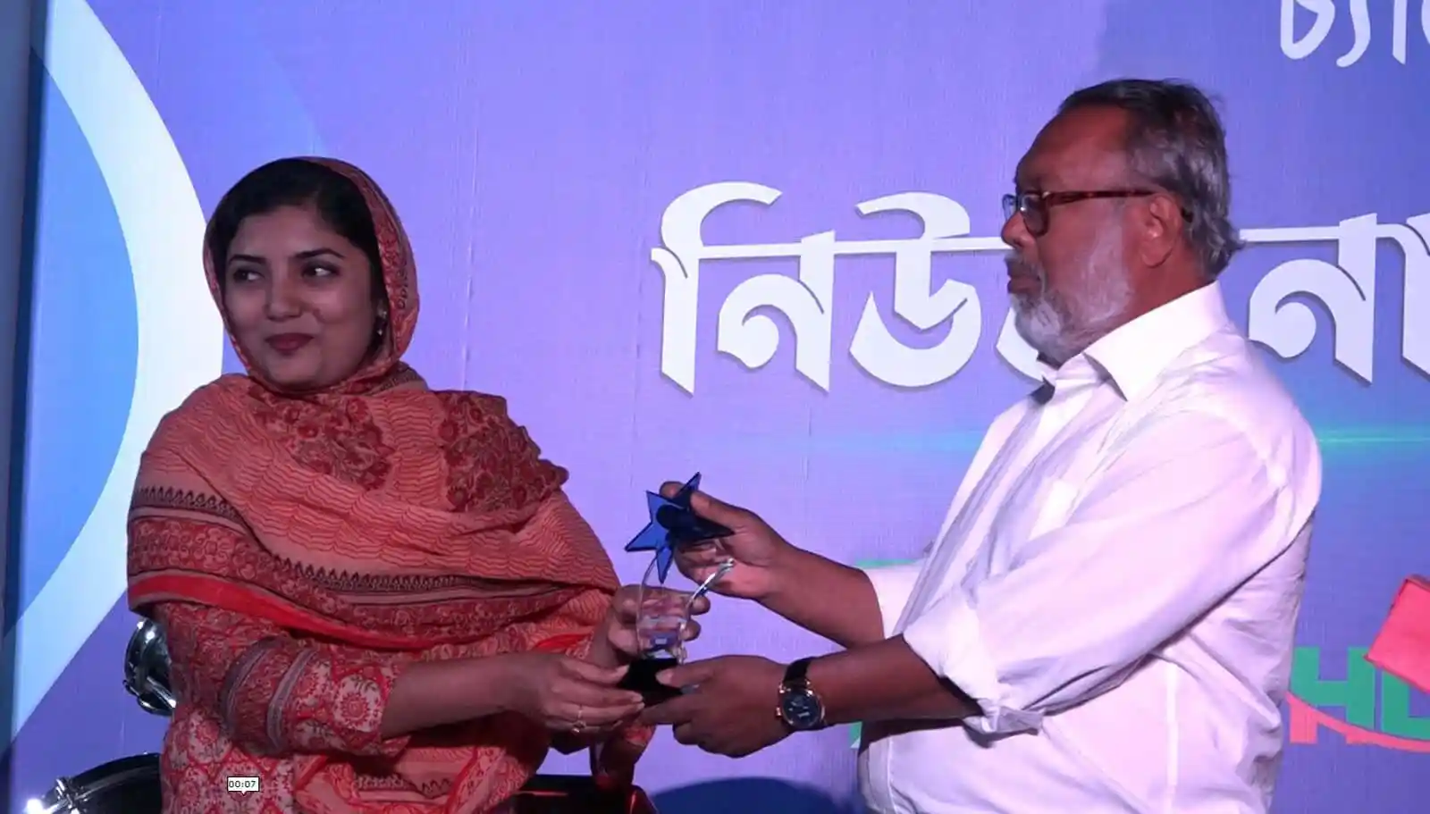 পুরস্কার গ্রহণ করছেন একজন নারী ও পুরুষ, অনুষ্ঠানে উপস্থিত. Channel i News - চ্যানেল আই নিউজ