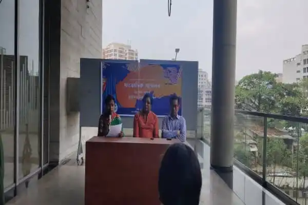 সংবাদ সম্মেলনে তিনজন বক্তা, পেছনে ব্যানার ও দর্শক. Channel i News - চ্যানেল আই নিউজ