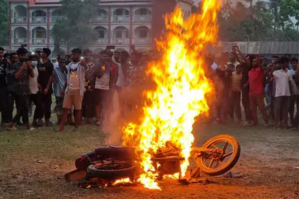 বিক্ষোভকারীরা আগুনে পুড়ে যাওয়া মোটরসাইকেল দেখছেন।. Channel i News - চ্যানেল আই নিউজ