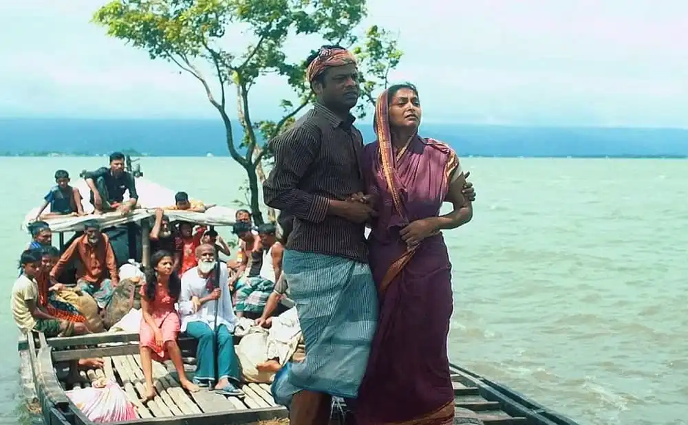 নদীর পাড়ে এক দম্পতি, পাশে অনেক মানুষ ও কাঠের নৌকা. Channel i News - চ্যানেল আই নিউজ