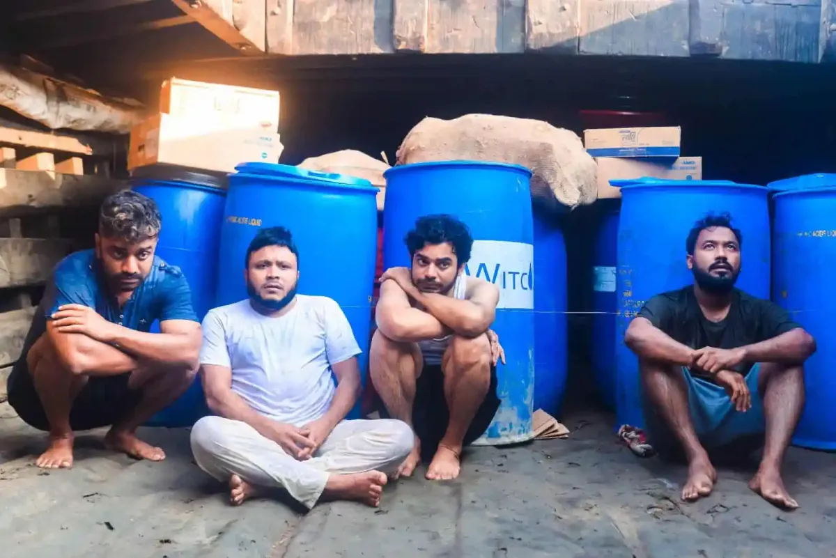 শ্রমজীবী মানুষরা বসে আছে কারখানার সামনে, পেছনে বড় বড় ড্রাম. Channel i News - চ্যানেল আই নিউজ