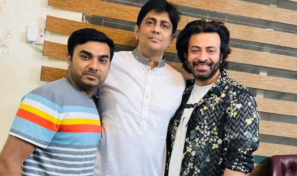 Three men posing together indoors, smiling at the camera. Channel i News - চ্যানেল আই নিউজ
