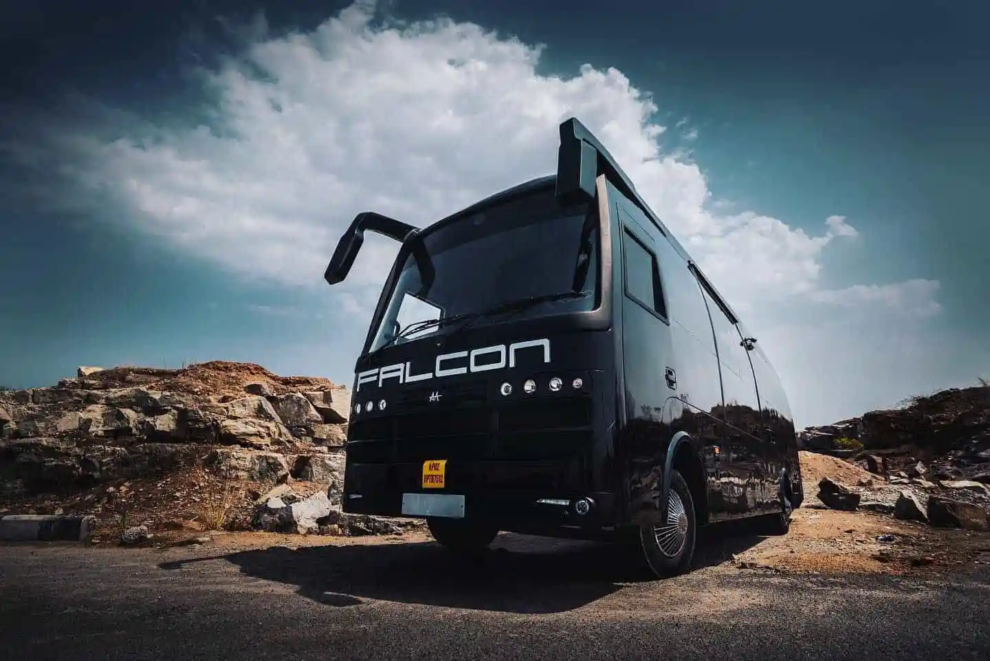 Black Falcon electric bus parked on rocky terrain under cloudy sky. Channel i News - চ্যানেল আই নিউজ