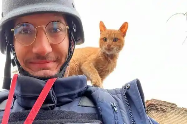 Man with helmet and glasses with orange cat on his shoulder outdoors. Channel i News - চ্যানেল আই নিউজ