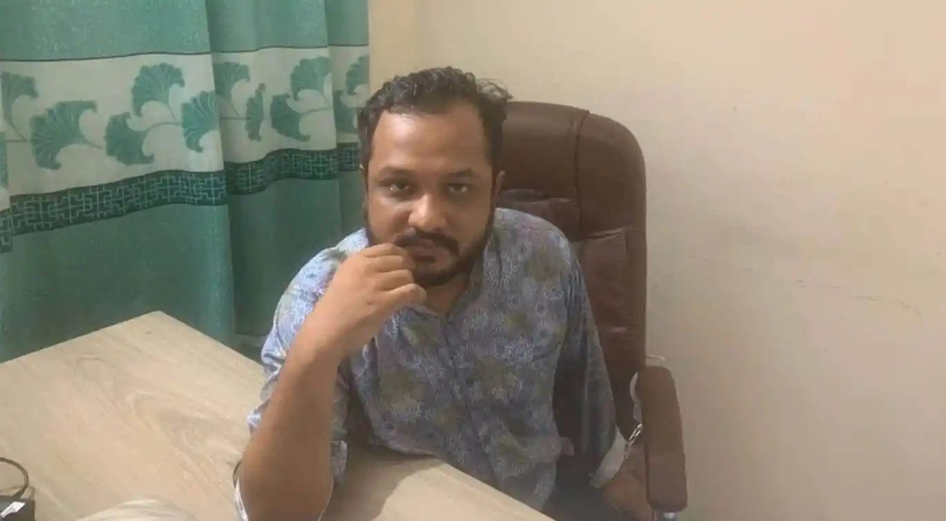 আদালত কক্ষে বসে একজন ব্যক্তি, পেছনে সবুজ পর্দা।. Channel i News - চ্যানেল আই নিউজ