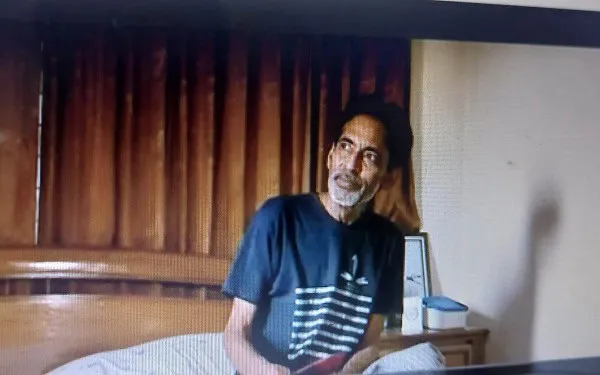 একজন পুরুষ ব্যক্তি ঘরে বসে, পেছনে কাঠের আলমারি ও টেবিল. Channel i News - চ্যানেল আই নিউজ