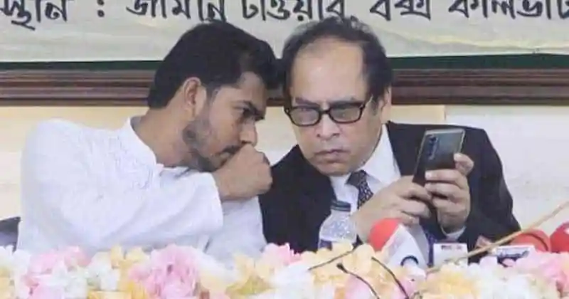 দুই ব্যক্তি মোবাইল ফোন দেখছেন, পত্রিকা ও ফুলের সাজে পরিবেশ. Channel i News - চ্যানেল আই নিউজ