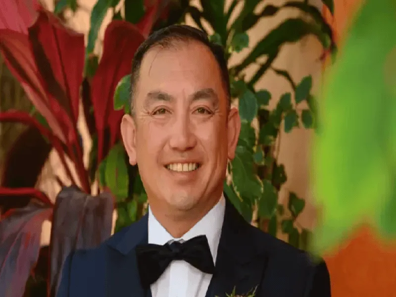 প্রফুল্ল হাস্যোজ্জ্বল ব্যক্তি, পটভূমিতে সবুজ গাছপালা. Channel i News - চ্যানেল আই নিউজ