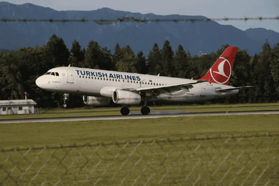 Turkish Airlines airplane landing on runway with mountains in background. Channel i News - চ্যানেল আই নিউজ