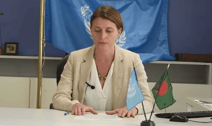 UN official in a beige blazer with UN and Bangladesh flags behind her. Channel i News - চ্যানেল আই নিউজ