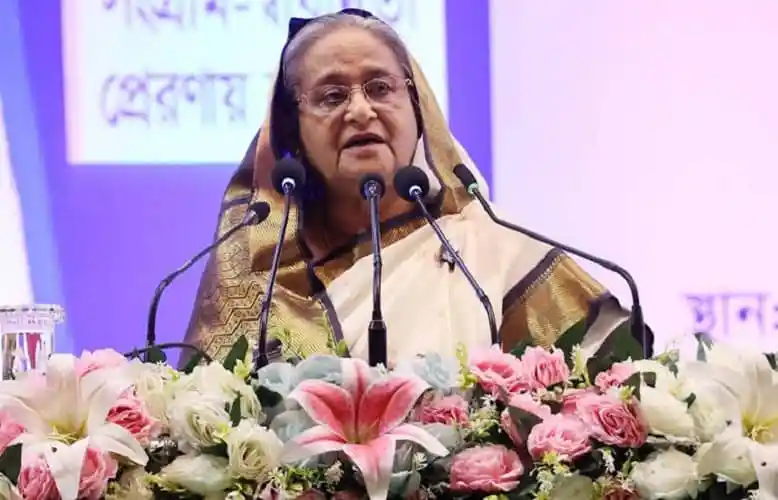 প্রধানমন্ত্রী শেখ হাসিনা ভাষণ দিচ্ছেন, ফুলের সামনে দাঁড়িয়ে. Channel i News - চ্যানেল আই নিউজ