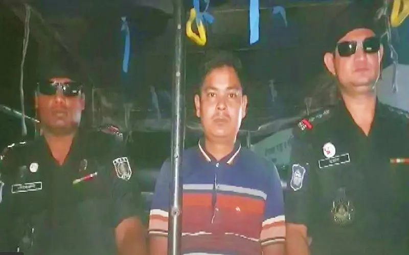 Arrested man flanked by police officers in uniform at night. Channel i News - চ্যানেল আই নিউজ