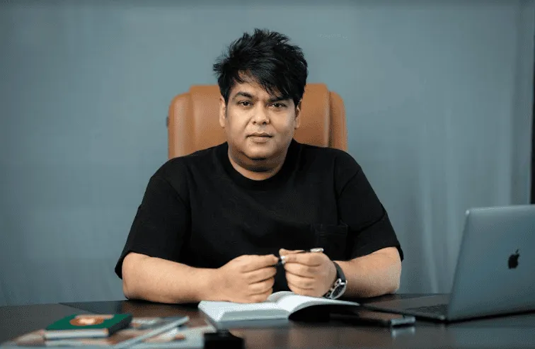 প্রফুল্ল মুখার্জি অফিসে বসে আছেন, ল্যাপটপ ও বইসহ. Channel i News - চ্যানেল আই নিউজ