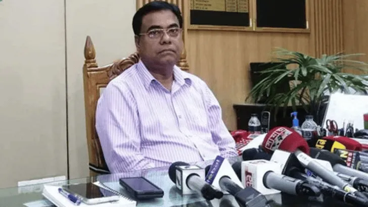 ইসি সচিবের ছবি, তিনি বসে আছেন, পেছনে গাছ ও অফিসের সাজসজ্জা. Channel i News - চ্যানেল আই নিউজ
