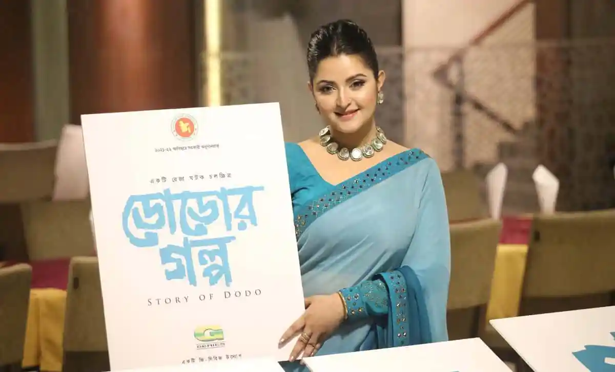 পরীমণি একটি বইয়ের সামনে দাঁড়িয়ে হাসিমুখে ছবি তুলছেন. Channel i News - চ্যানেল আই নিউজ