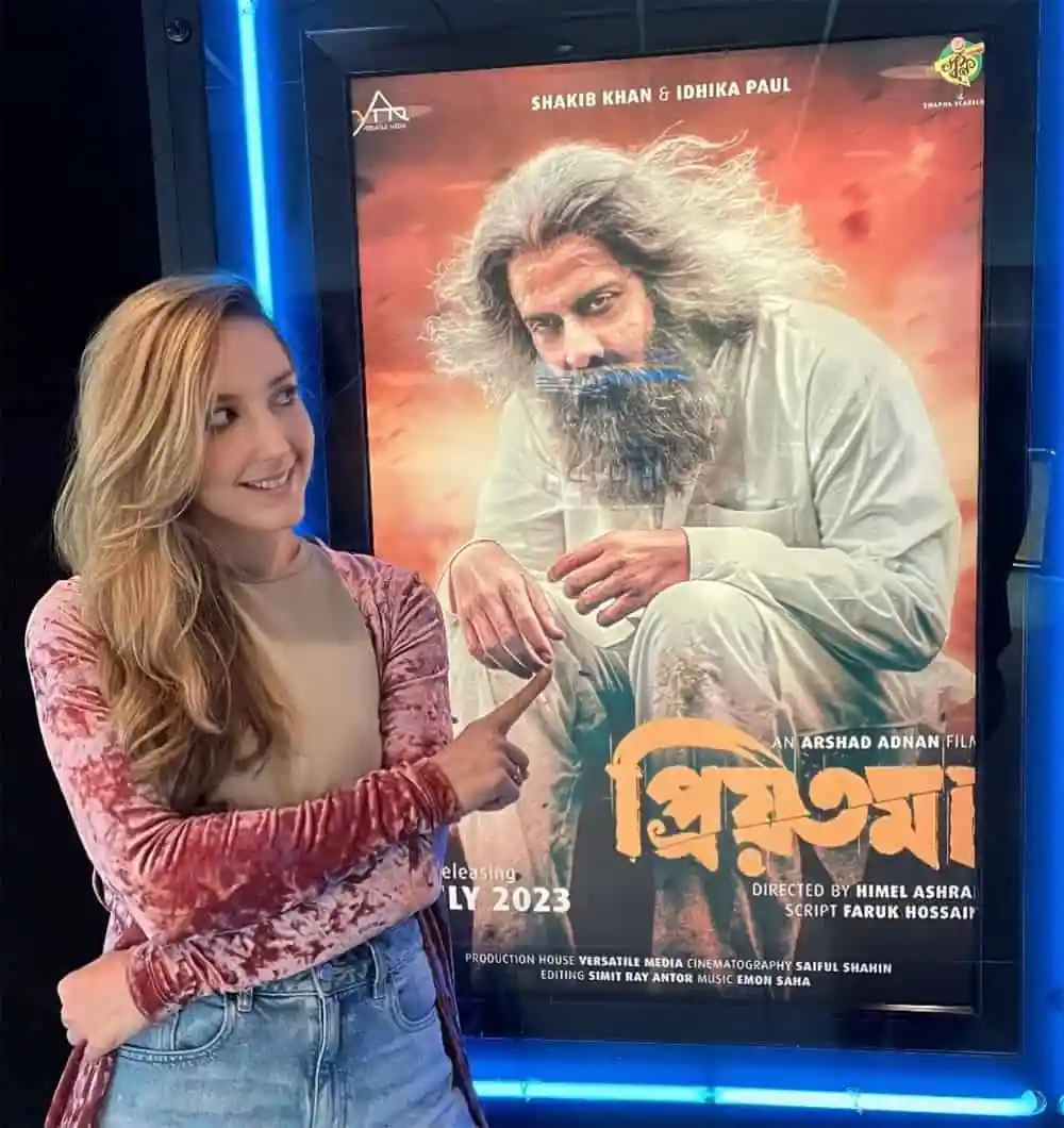 অভিনেত্রী রাজকুমার সিনেমার পোস্টারের সামনে দাঁড়িয়ে হাসছেন. Channel i News - চ্যানেল আই নিউজ