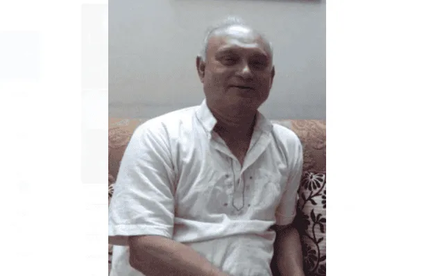 বৃদ্ধ ব্যক্তি হাসিমুখে বসে আছেন, পটভূমিতে সোফা ও দেয়াল. Channel i News - চ্যানেল আই নিউজ