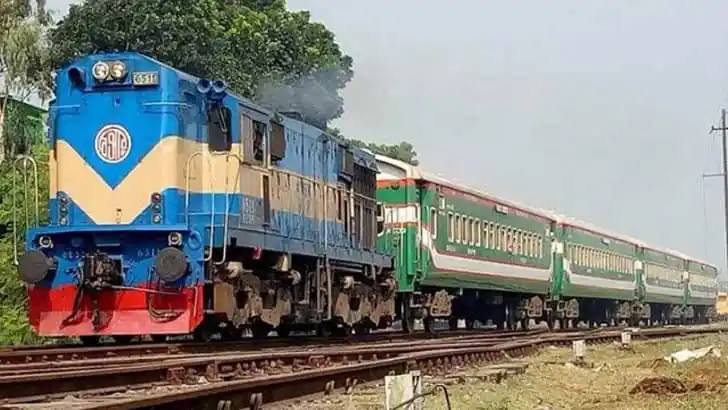 একটি ট্রেন রেললাইনে চলন্ত অবস্থায়, পেছনে সবুজ গাছপালা. Channel i News - চ্যানেল আই নিউজ