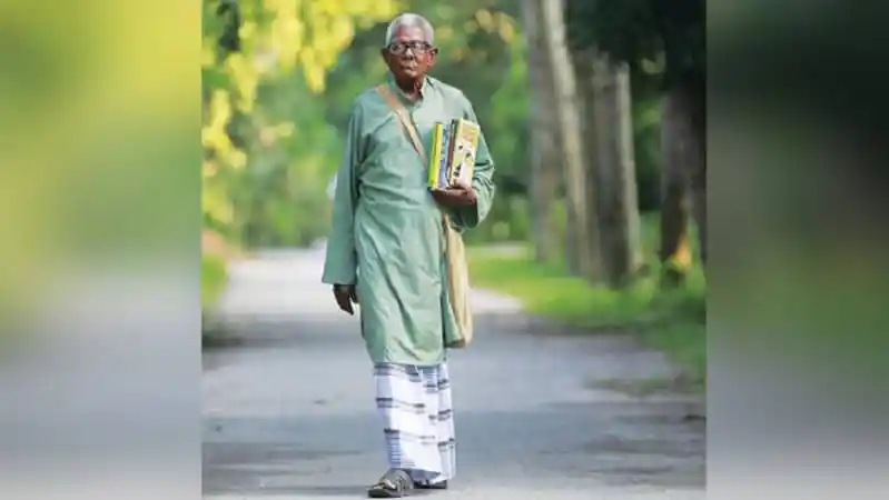 বৃদ্ধ ব্যক্তি বই নিয়ে হাঁটছেন, প্রকৃতির মাঝে শান্তিপূর্ণ পরিবেশে. Channel i News - চ্যানেল আই নিউজ