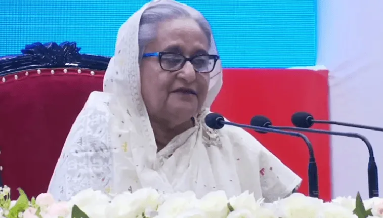 প্রধানমন্ত্রী ভাষণ দিচ্ছেন, পেছনে বাংলাদেশ পতাকা ও ডিজিটাল স্ক্রিন. Channel i News - চ্যানেল আই নিউজ