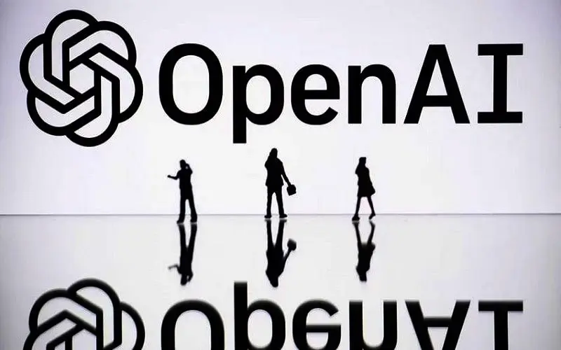 OpenAI logo with silhouettes of people walking in front of it. Channel i News - চ্যানেল আই নিউজ