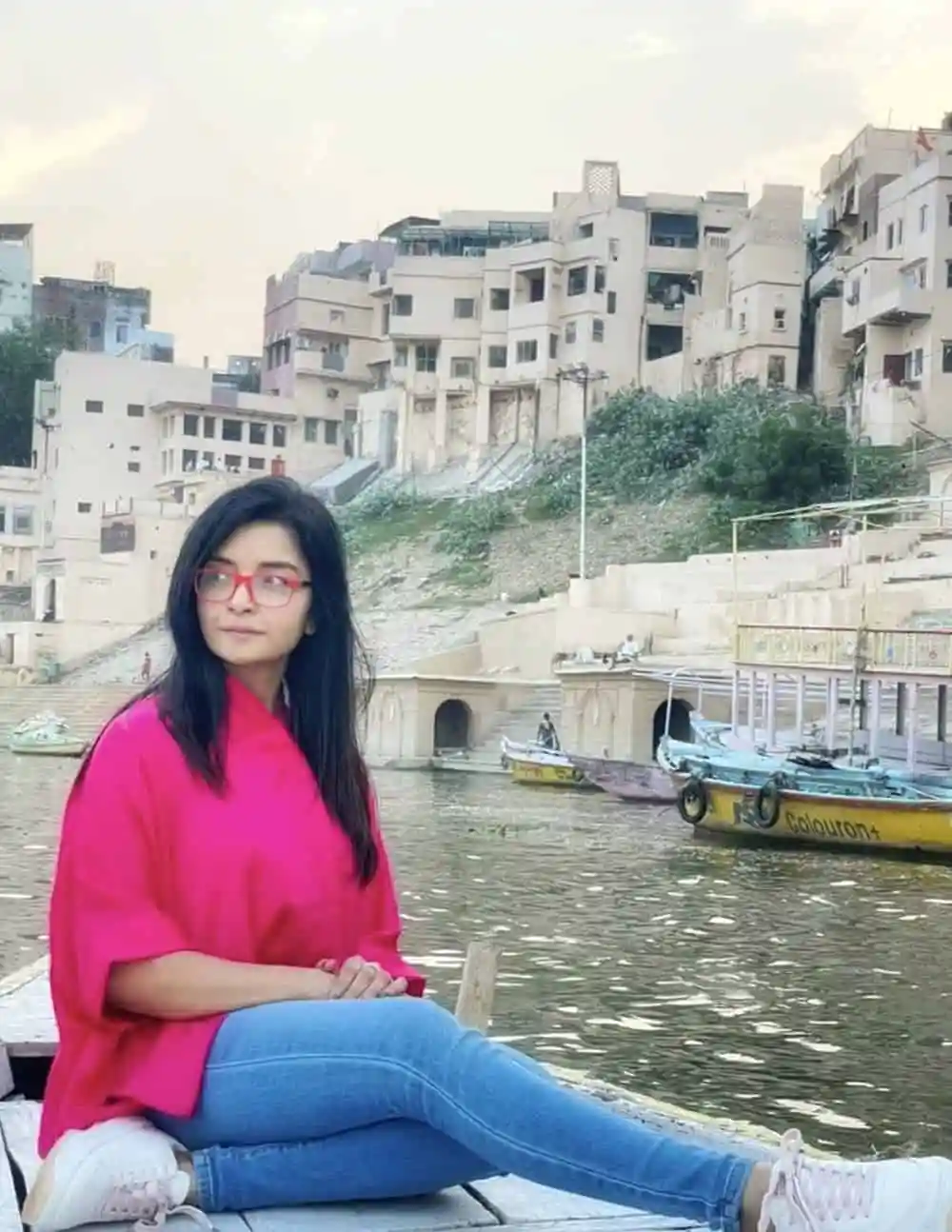 নদীর পাশে বসে থাকা তরুণী, শহরের পটভূমিতে আধুনিক বাড়ি ও জলযান. Channel i News - চ্যানেল আই নিউজ