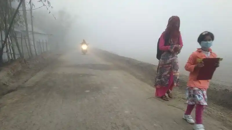 ধূসর সকালে রাস্তায় দুই নারী, একজন মাস্ক পরা, অন্যজন বই নিয়ে হাঁটছেন. Channel i News - চ্যানেল আই নিউজ