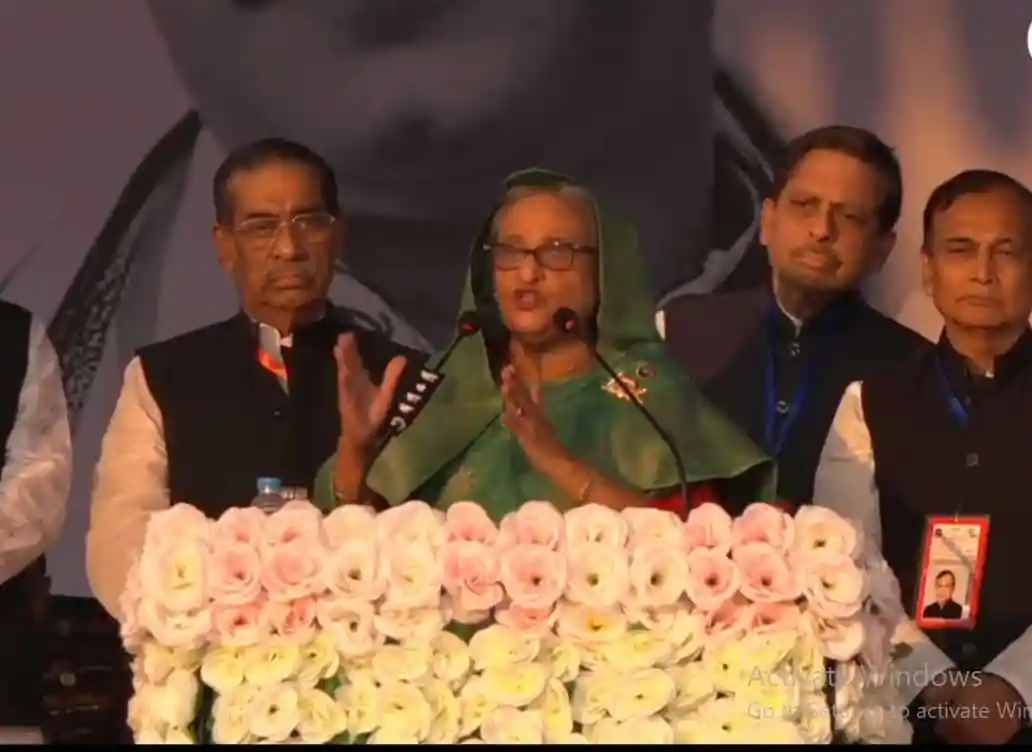 শেখ হাসিনা বক্তৃতা দিচ্ছেন, পাশে অন্য নেতারা উপস্থিত. Channel i News - চ্যানেল আই নিউজ