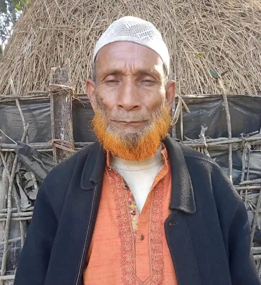 বৃদ্ধ ব্যক্তি মাথায় পাগড়ি ও গোঁফে রঙিন দাড়ি, ধানের খেতের পাশে দাঁড়িয়ে. Channel i News - চ্যানেল আই নিউজ
