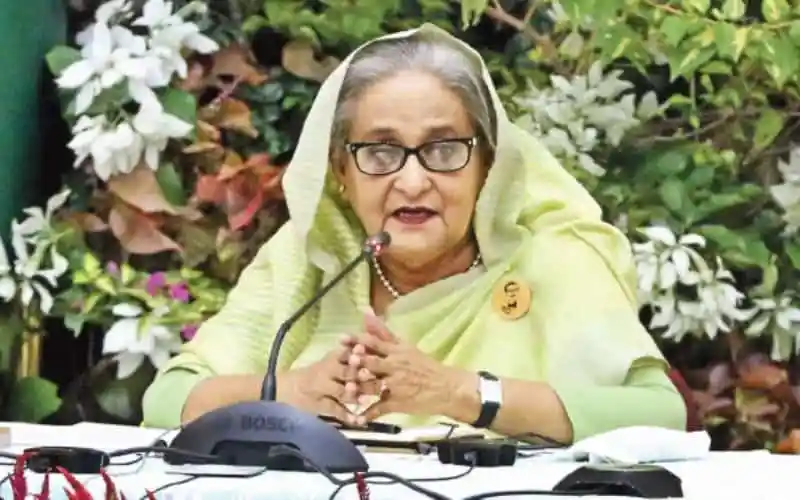 শেখ হাসিনা সংবাদ সম্মেলনে বক্তৃতা দিচ্ছেন, ফুলের পটভূমিতে. Channel i News - চ্যানেল আই নিউজ