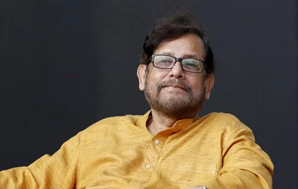 আসাদুজ্জামান নূর হাসিমুখে বসে থাকছেন, পর্দার পেছনে কালো ব্যাকড্রপ. Channel i News - চ্যানেল আই নিউজ