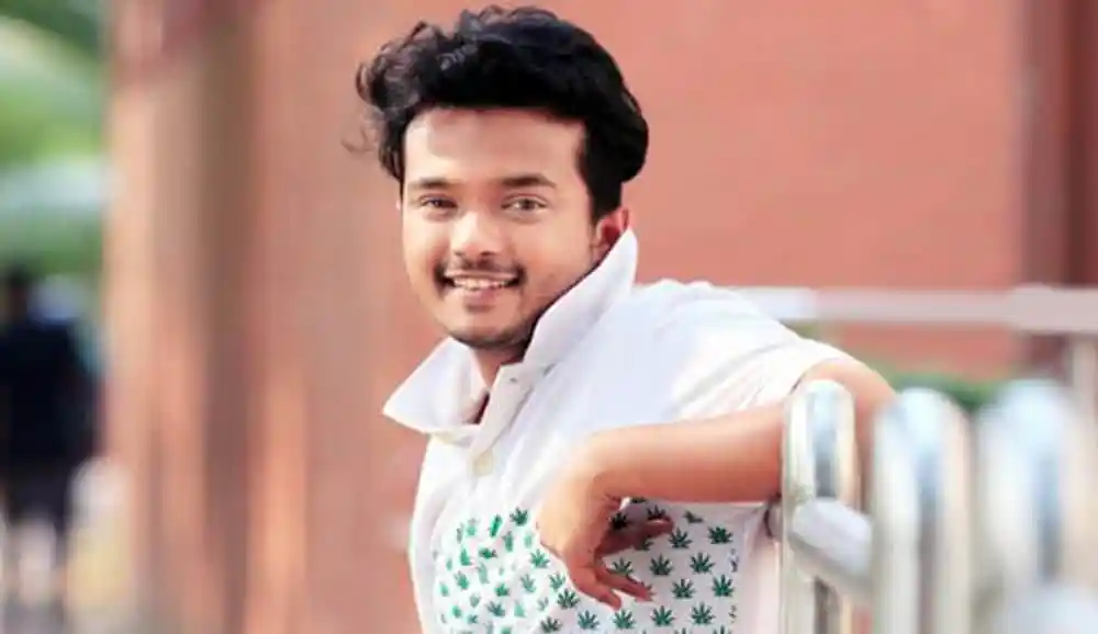 অ্যালেন শুভ্র হাসিমুখে দাঁড়িয়ে আছেন, ব্যাকগ্রাউন্ডে ব্রিটিশ স্থাপনা. Channel i News - চ্যানেল আই নিউজ
