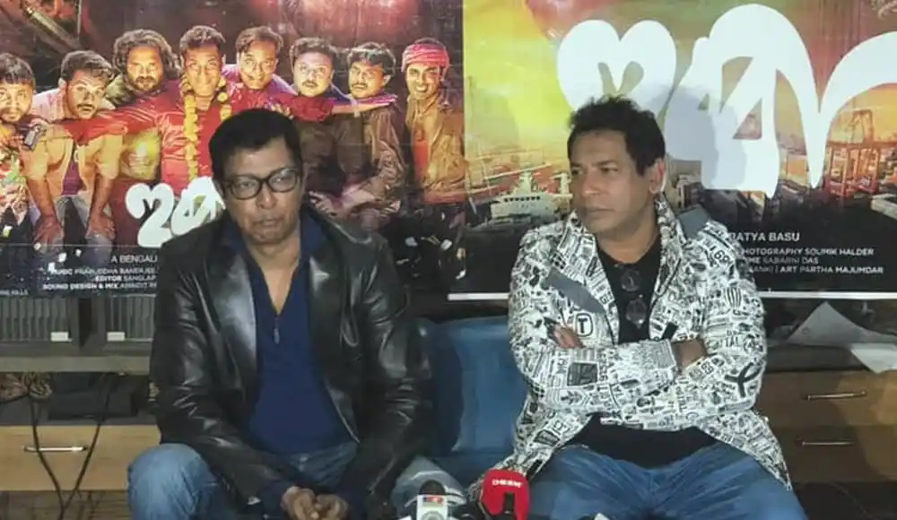 দুইজন সাংবাদিক সংবাদ সম্মেলনে বসে, পেছনে সিনেমার পোস্টার. Channel i News - চ্যানেল আই নিউজ