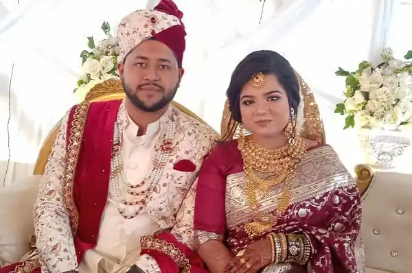 বিবাহিত দম্পতি সাদা ও লাল পোশাকে, ফুলের পেছনে বসে. Channel i News - চ্যানেল আই নিউজ